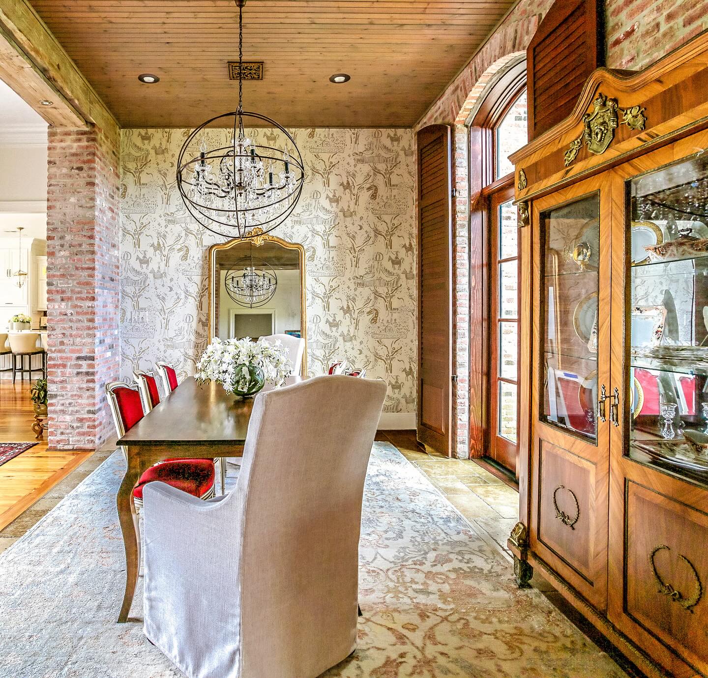 Dining room with exposed brick, a gilt-framed antique French mirror and a burl-wood display cabinet from DOP Antiques