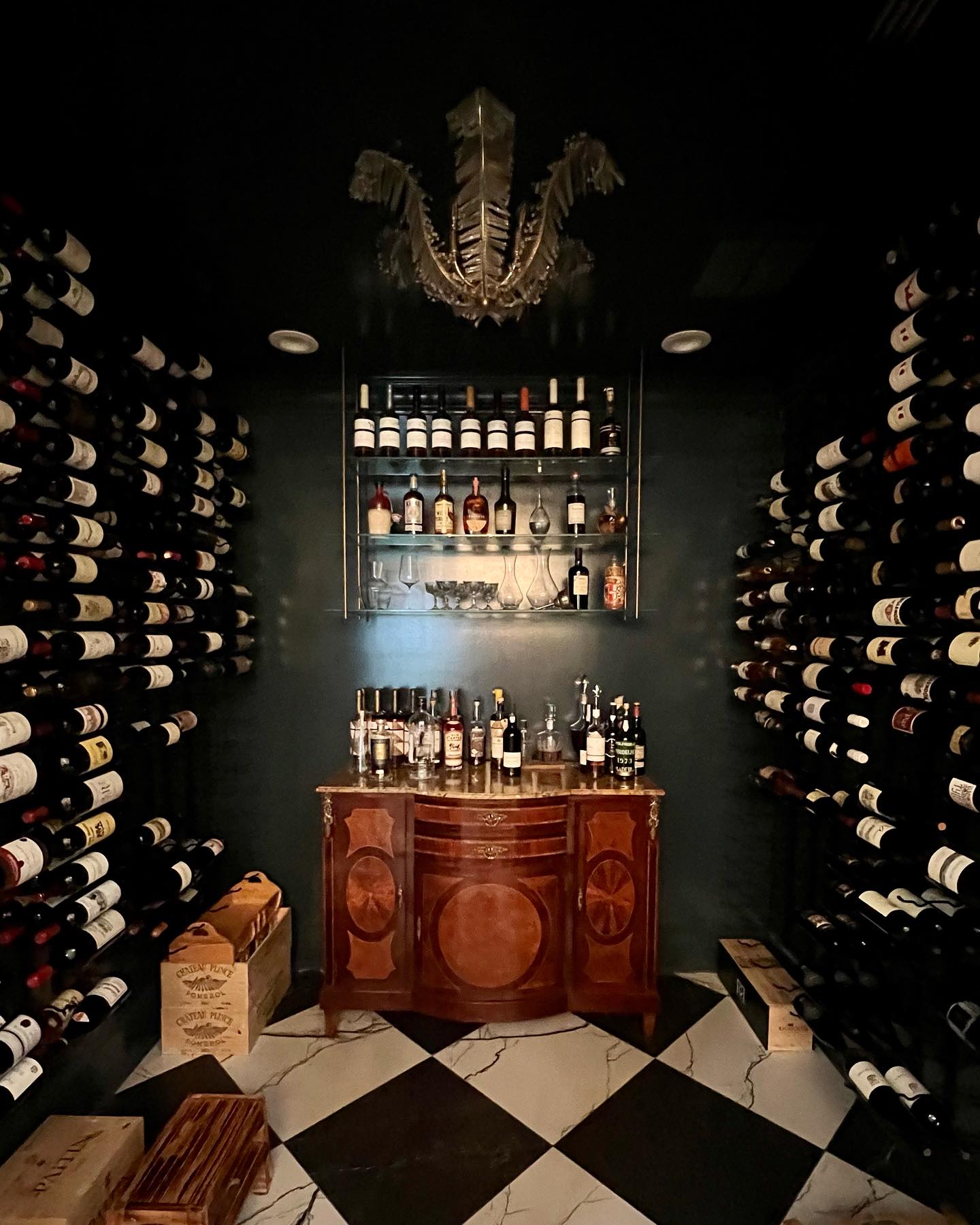 Dark green wine cellar with a marble-topped inlaid mahogany commode and a plume-form crystal chandelier over harlequin marble floors