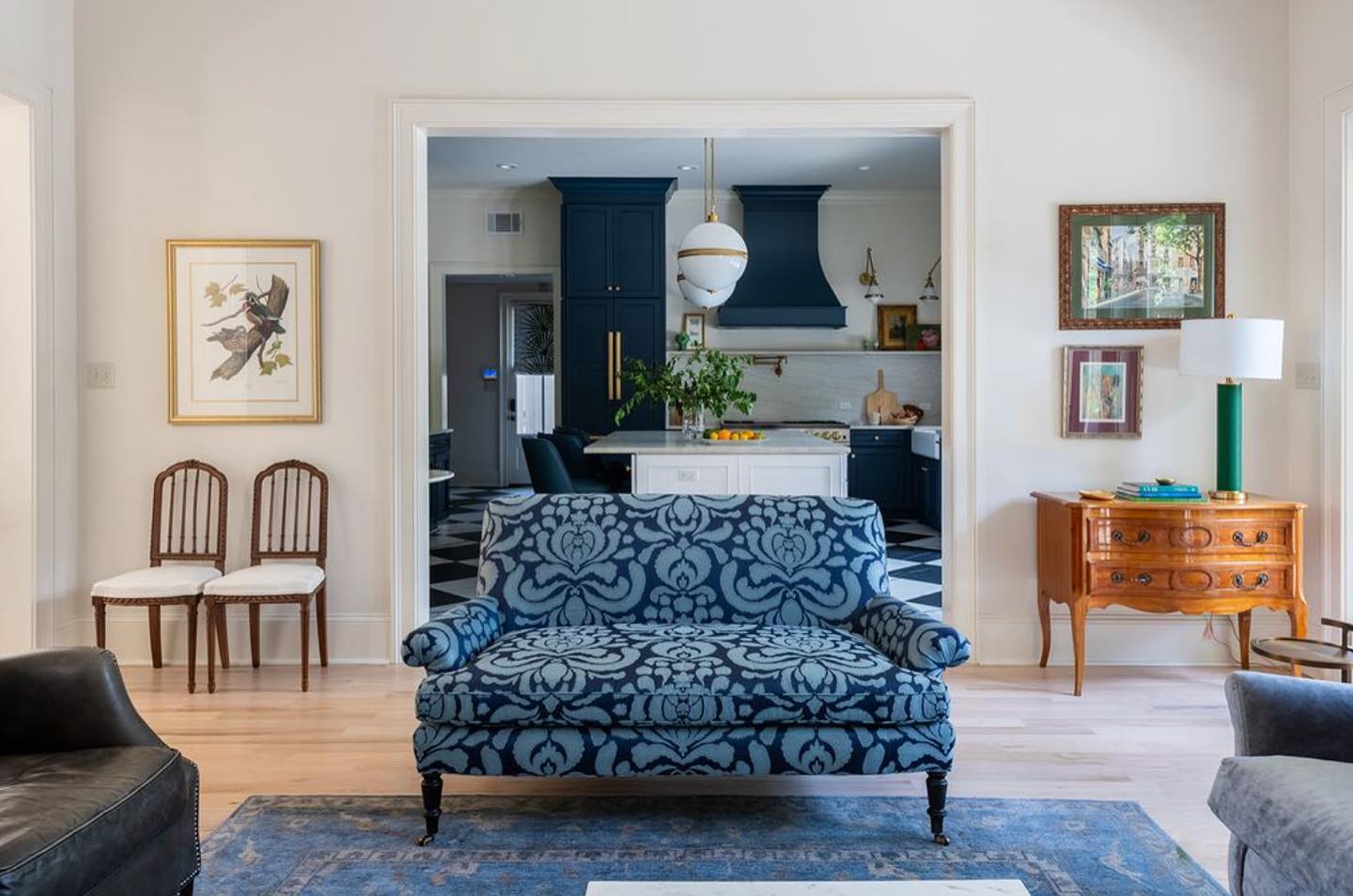 Living room opening to a navy kitchen, with a fruitwood bombé commode and antique carved side chairs from DOP Antiques