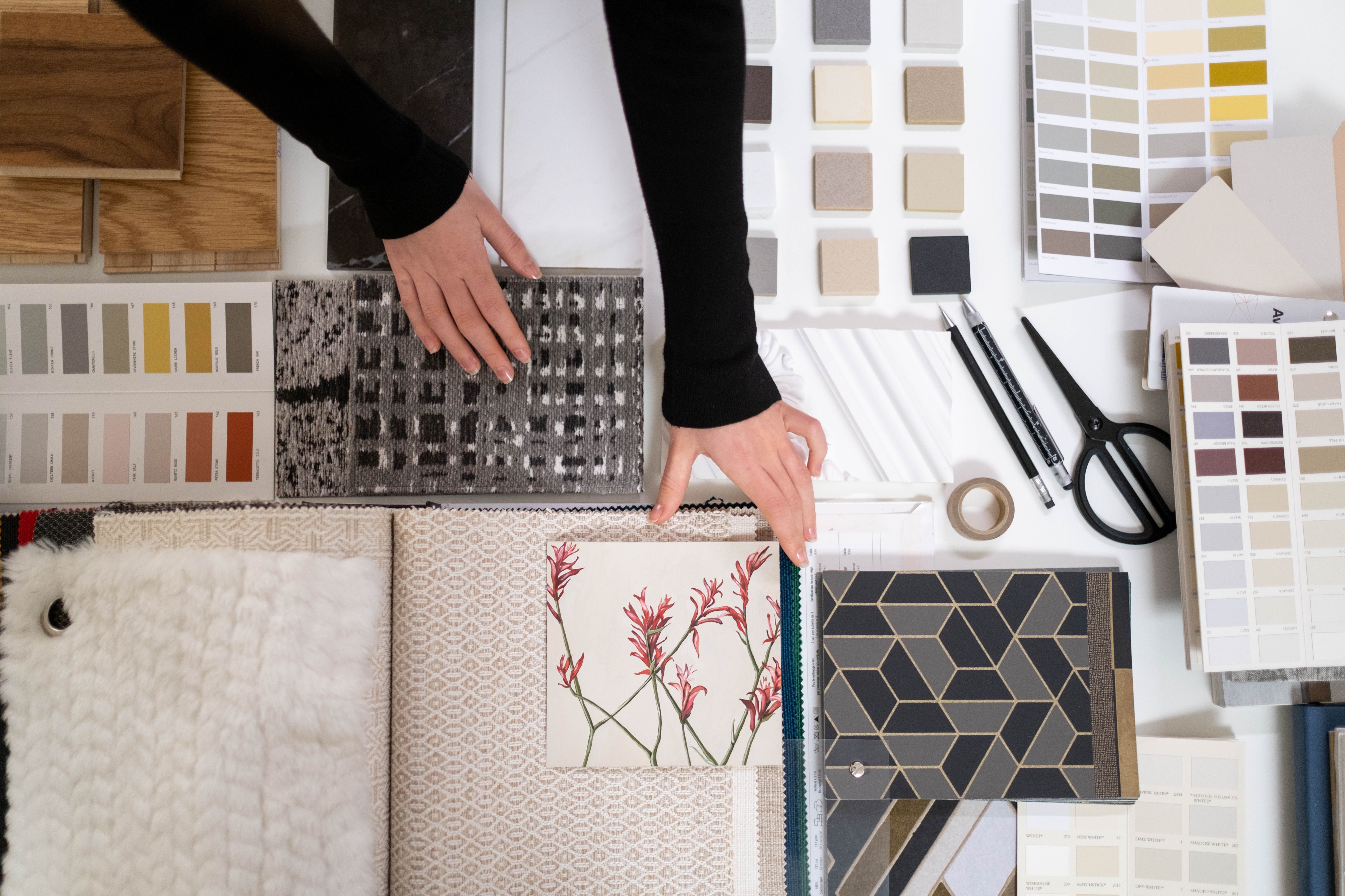 Hands arranging fabric, wood, paint and moulding samples on an interior design worktable.