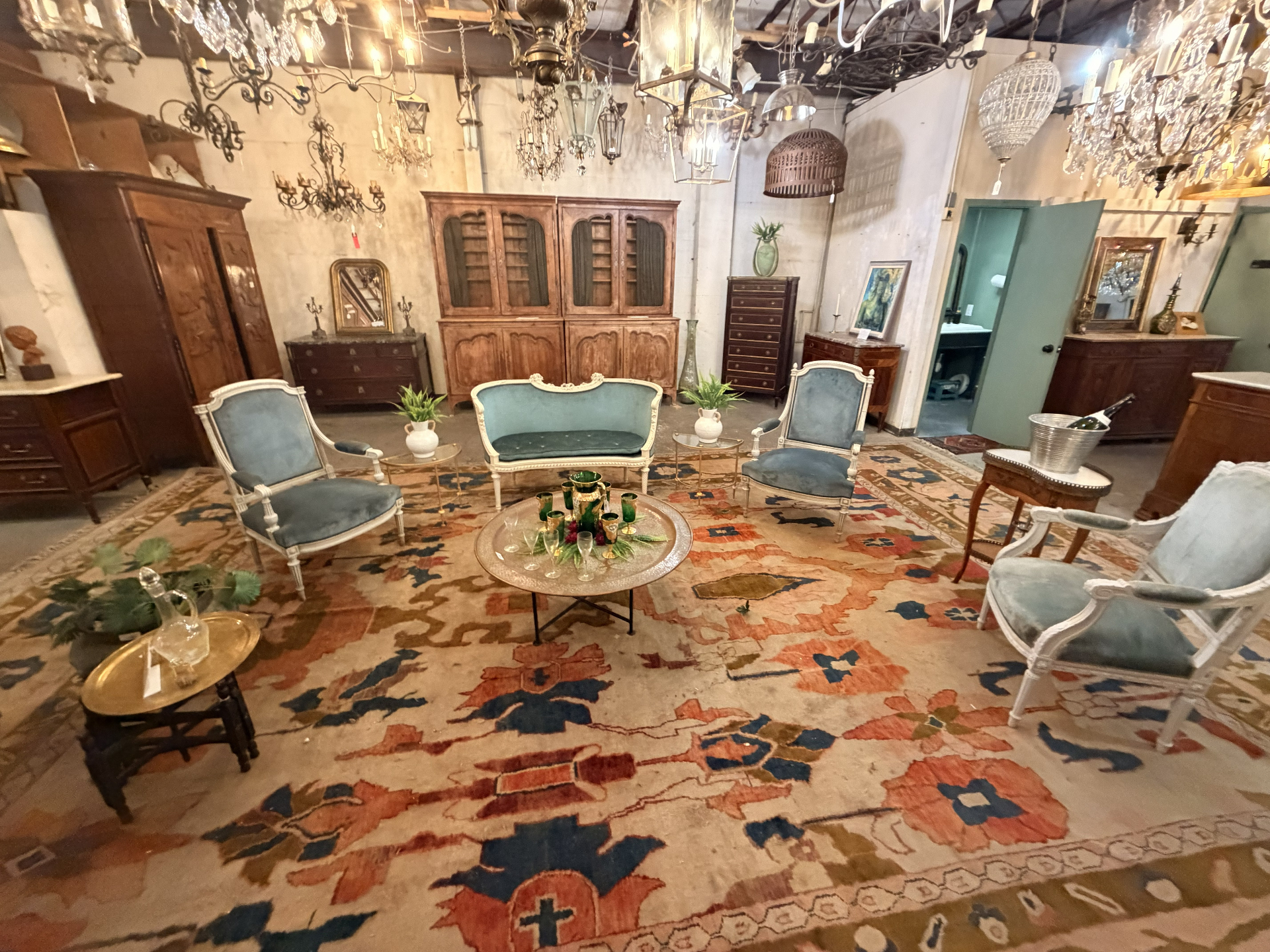 A vignette of blue velvet Louis-style chairs and settee on an antique rug beneath chandeliers