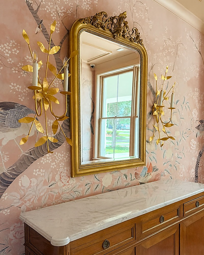 Powder room with hand-painted pink chinoiserie walls, a gilt Louis Philippe mirror and gold leaf sconces above a marble-topped antique commode