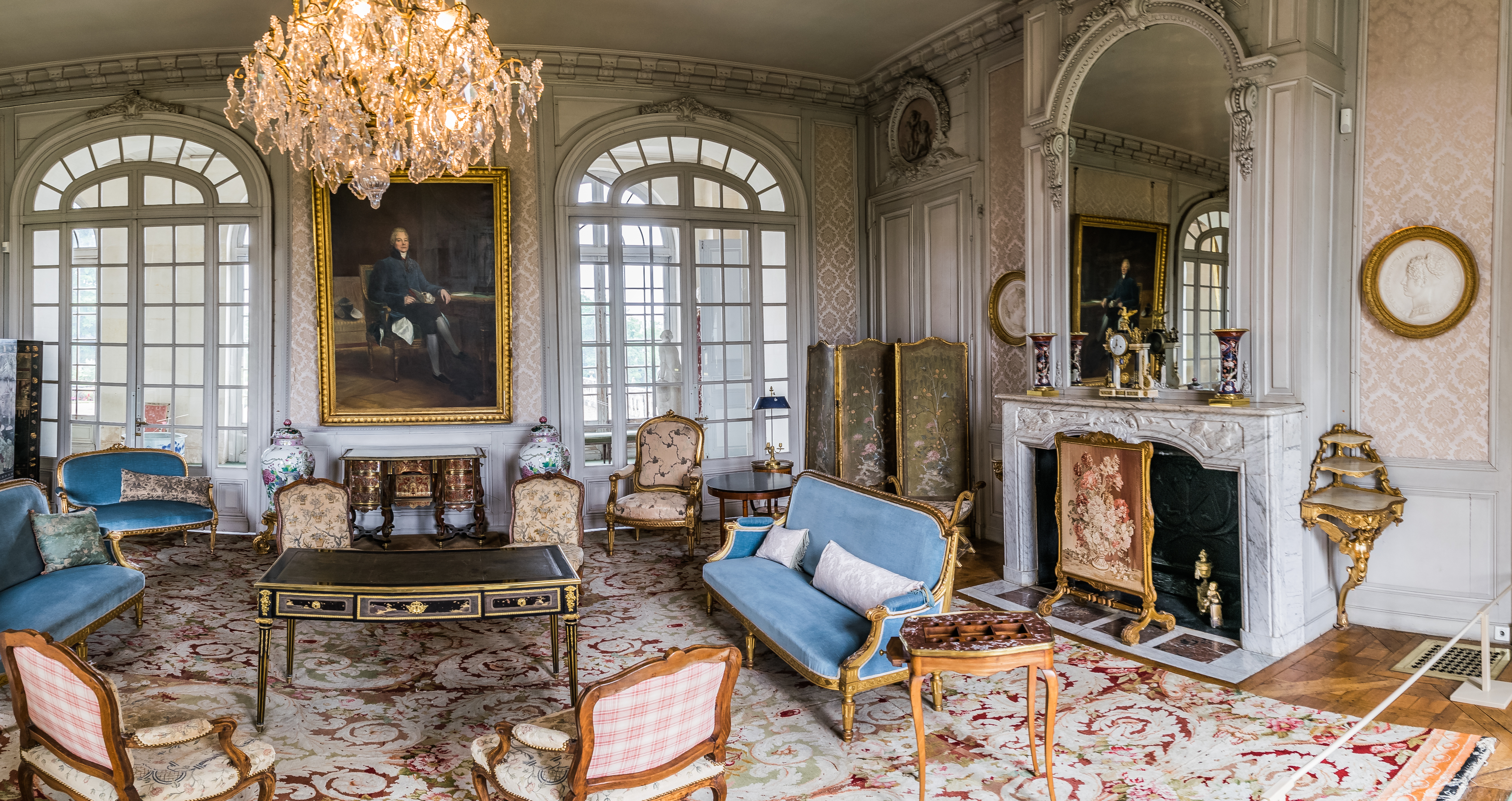 Blue Room at Château de Valençay in France, furnished with antique seating, a writing desk, a commode, mirrors and a chandelier.