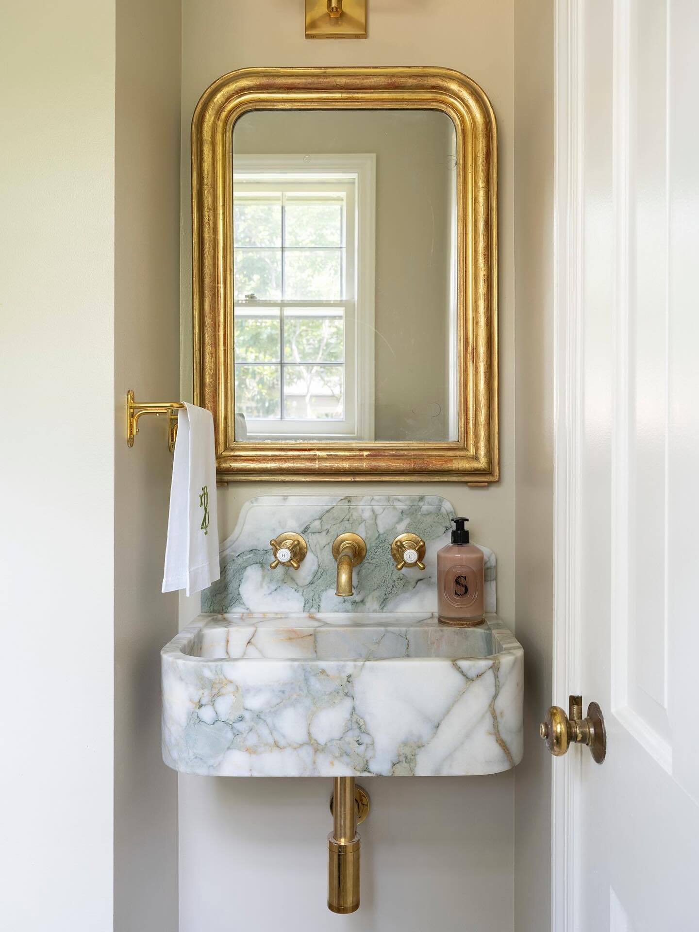 Powder room with a gold-leaf Louis Philippe mirror above a marble wall-mounted sink with unlacquered brass fittings